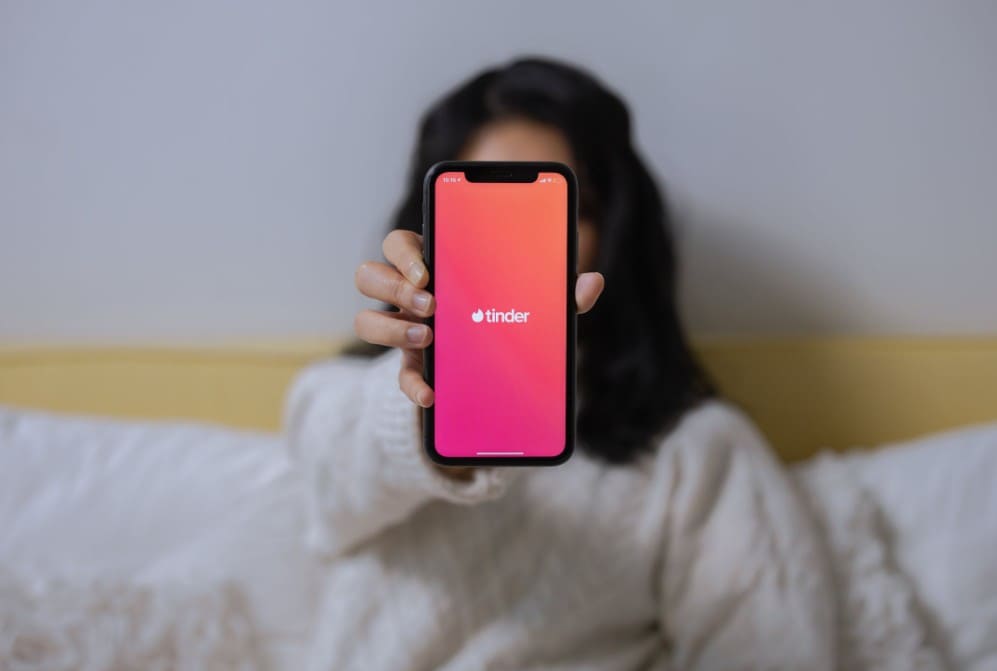 An image of a woman holding a phone with the Tinder logo showing