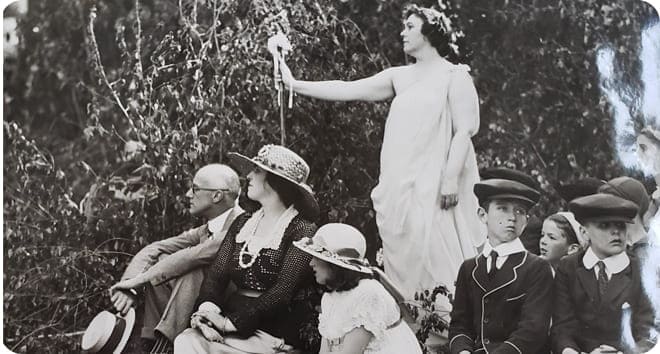 A group of women and children in costumes sit and stand outdoors during a fundraising celebration in Scarsdale in the early 20th century.